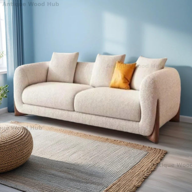 Beige sofa with a yellow pillow in a room with a blue wall and a textured rug.