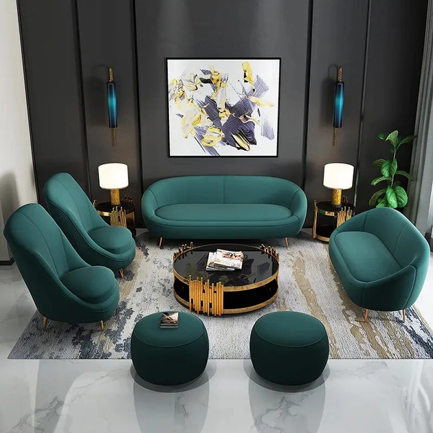 An elegant emerald green 9-seater sofa set with velvet upholstery, consisting of a three-seater sofa, a two-seater sofa, two single seater chairs, two round puff stools, and a designer coffee table, placed in a modern living room setting with marble flooring and decorative lighting.