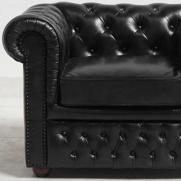 Black leather Chesterfield sofa with tufted backrest on a light wooden floor.