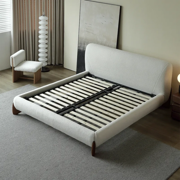 Contemporary low-profile bed frame with a rounded, white boucle upholstered headboard and base, showcasing the internal wooden mattress support slats and angled wood feet.