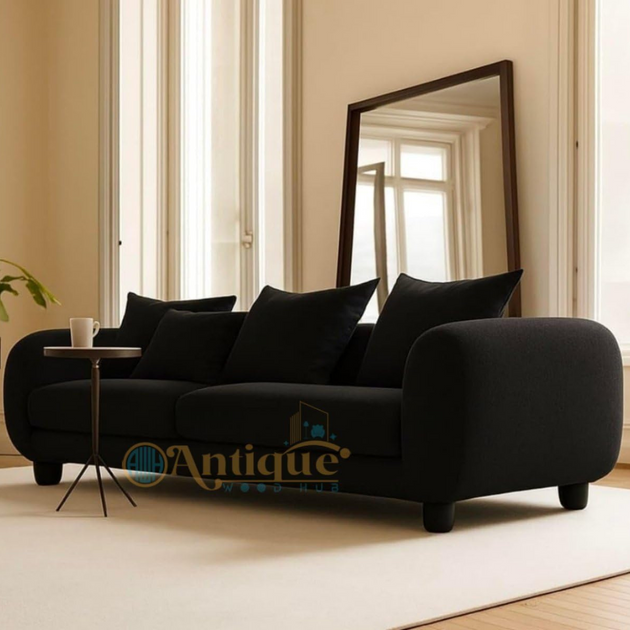 Black sofa with cushions in a room with large mirror and light-colored walls.