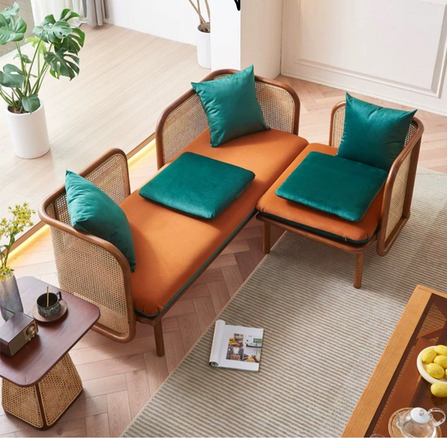 Top view of a modern rattan-framed sofa set with orange cushions and teal pillows, paired with a matching side table and indoor plants in a bright contemporary living room