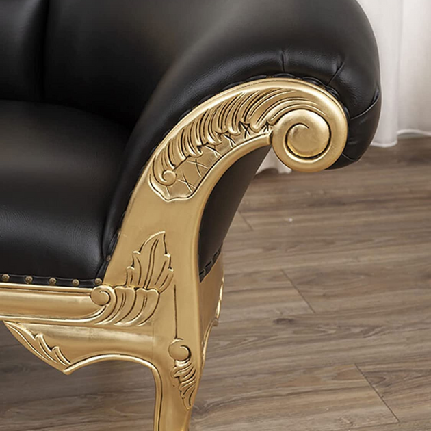 Black leather chair with gold ornate armrests on a wooden floor.